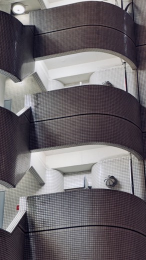 Architectural photo looking up at curved, tiled balcony walls and a spiral stairwell inside a building interior.